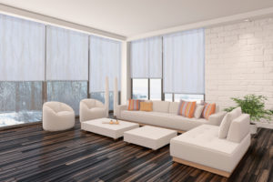 Modern minimalist sitting room interior with a bare wooden parquet floor, contemporary upholstered lounge suite and large view windows with a garden view in a white brick wall